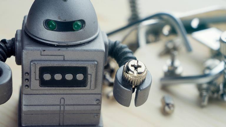 AI in Outsourced Marketing: Robot Holding Screw for Hiring Tips Close-up of a silver toy robot holding a small screw in its claw, with other mechanics blurred in the background.