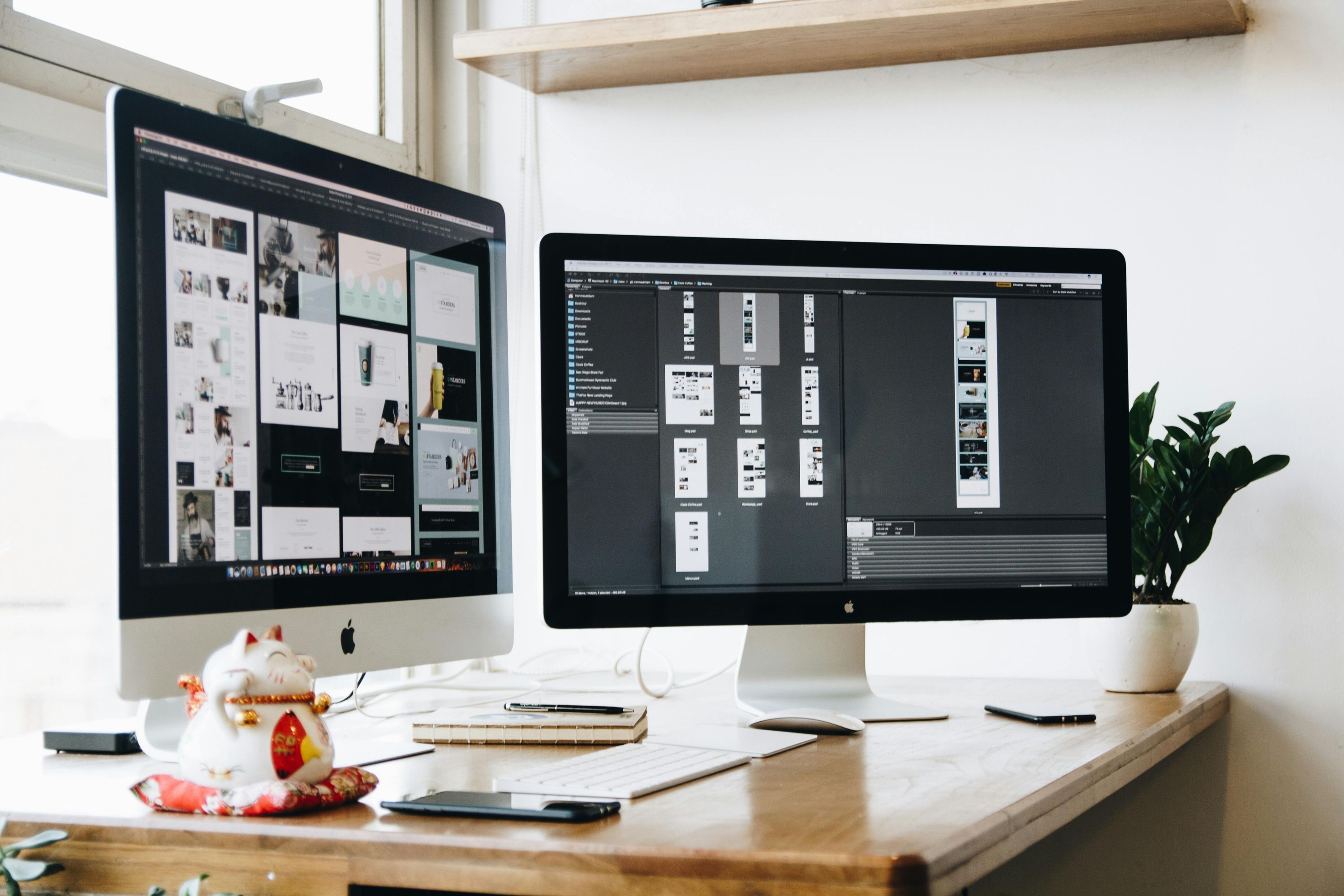 Well-organized marketing team workspace with two desktop computers displaying web designs, a Maneki-neko figurine, and a green plant, symbolizing growth and digital strategy.