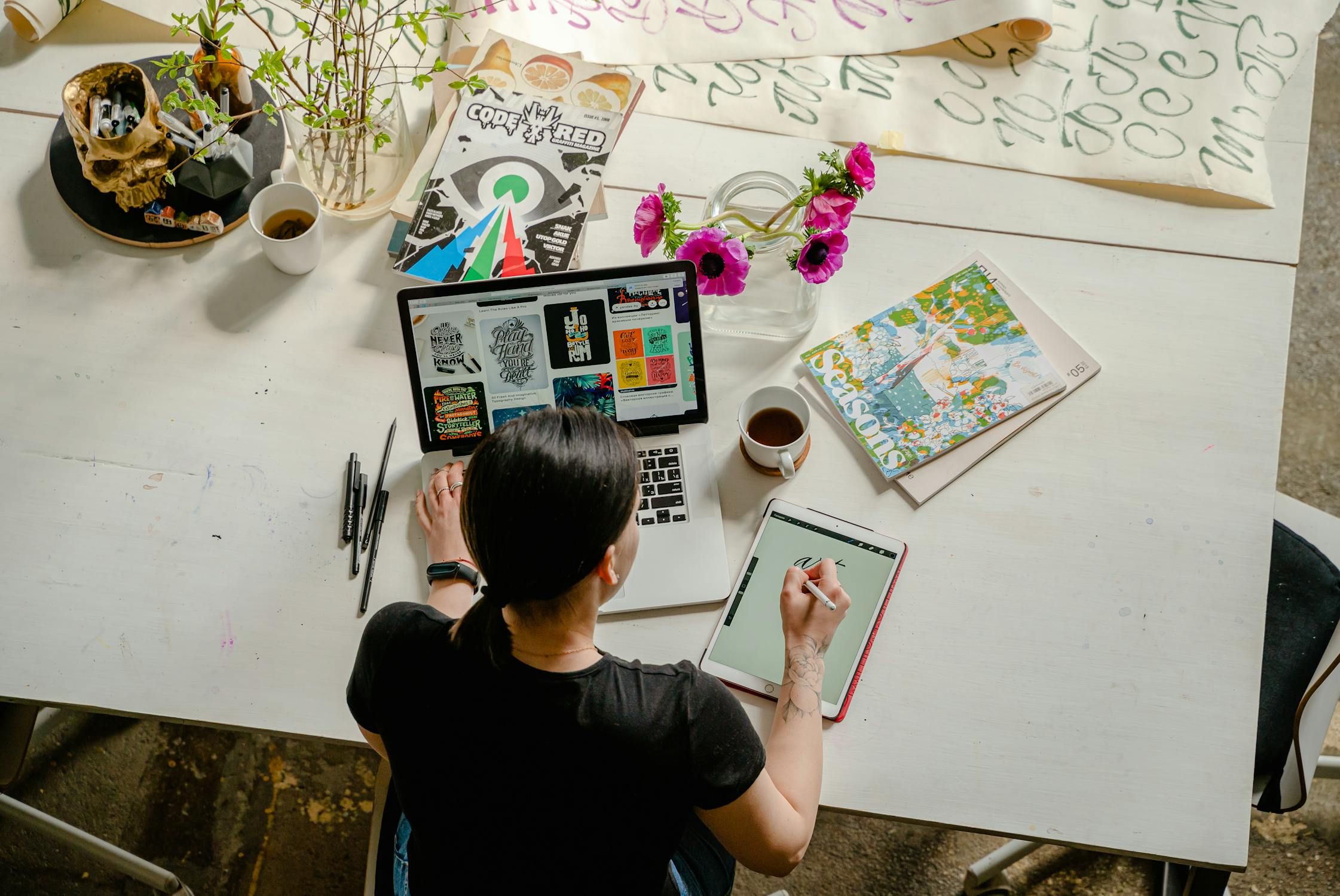 Creative marketing contractor working on laptop and drawing tablet, surrounded by design tools and plants.