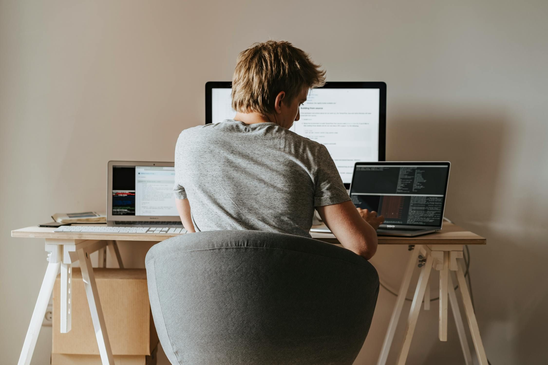 Man working attentively at a desk with two laptops and a large monitor, demonstrating focus on digital tasks.