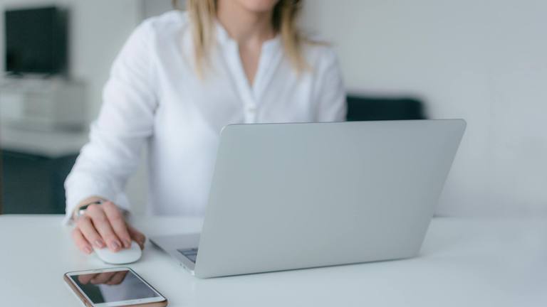 Remote Freelance Marketing Consultant Working A woman working remotely at a desk, using a white mouse next to an open laptop and a smartphone.