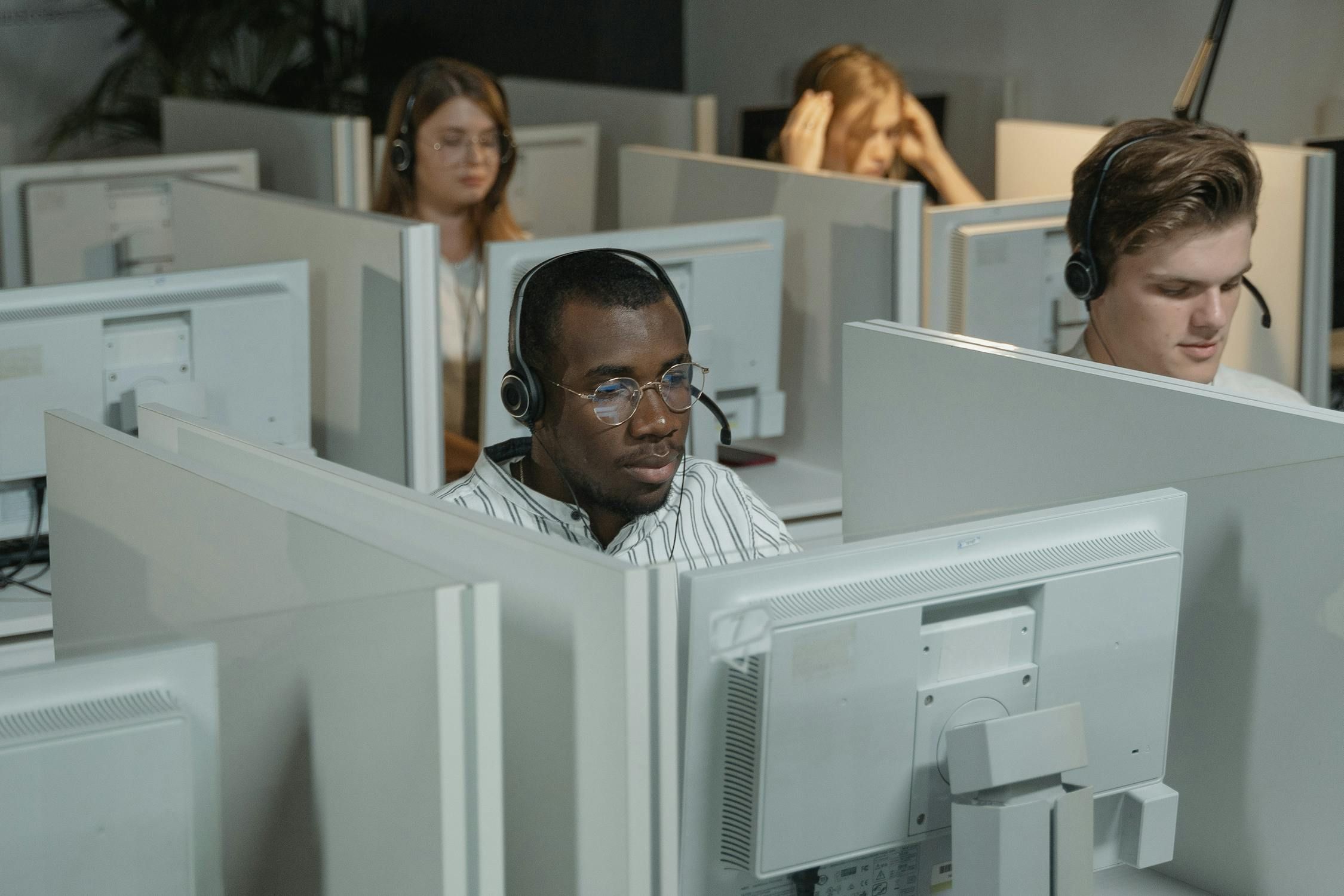 A diverse group of call center agents wearing headsets, focused on their computer screens in a modern office with cubicles.