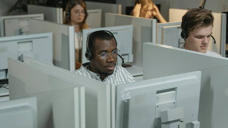 Remote Talent & Outsourced Support for Marketing A diverse group of call center agents wearing headsets, focused on their computer screens in a modern office with cubicles.