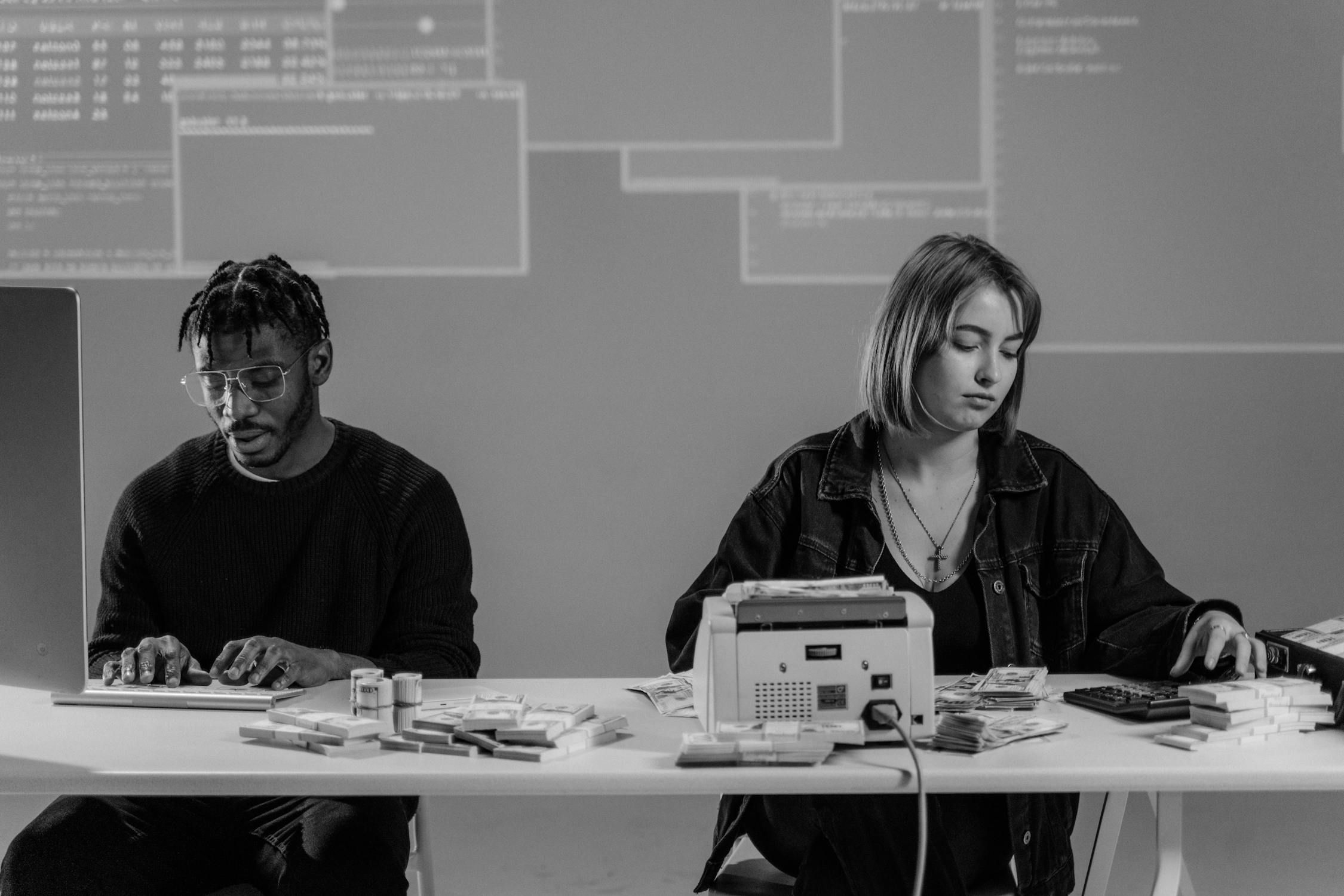 A man typing on a computer and a woman counting money with a machine, both engaged in back-office tasks, representing efficient remote staffing.
