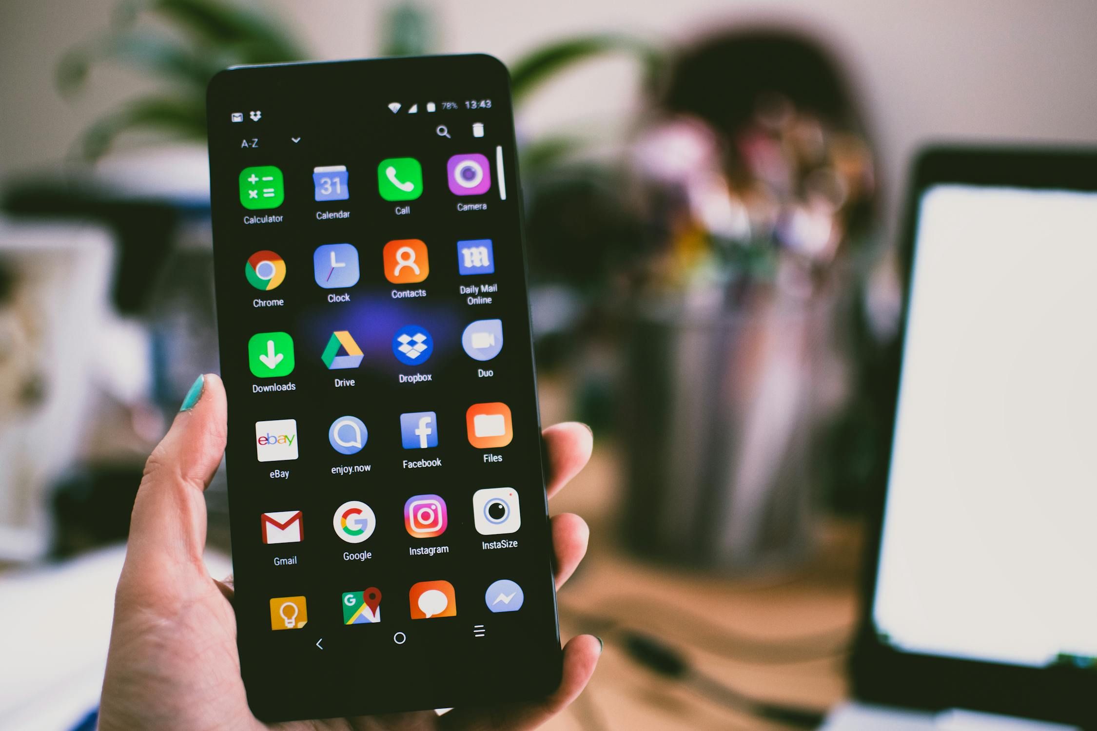 A hand holds a smartphone displaying various app icons on its screen, including social media, productivity, and web browsing applications.