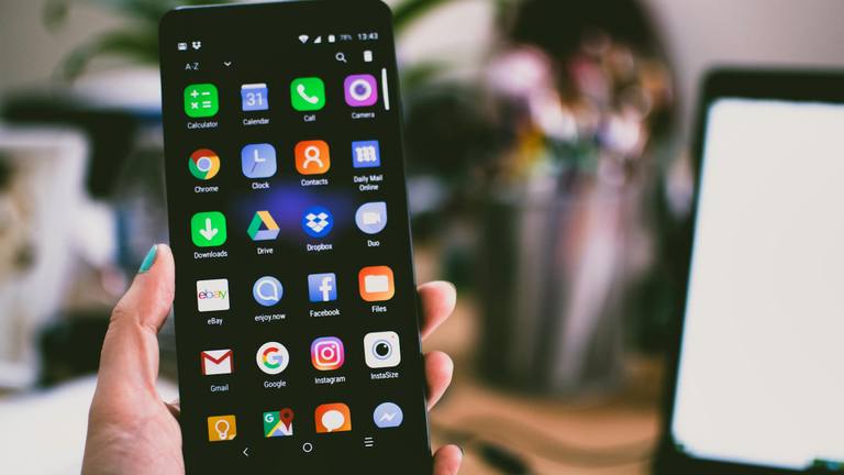 Marketing Team Structure and Digital App Usage A hand holds a smartphone displaying various app icons on its screen, including social media, productivity, and web browsing applications.
