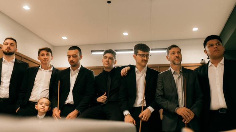 Serious Businessmen in Suits with Pool Cues | Outsourcing Marketing 2026 Seven men, one boy, all dressed in formal attire including suits and ties, stand or sit, looking upwards with serious expressions, holding pool cues.